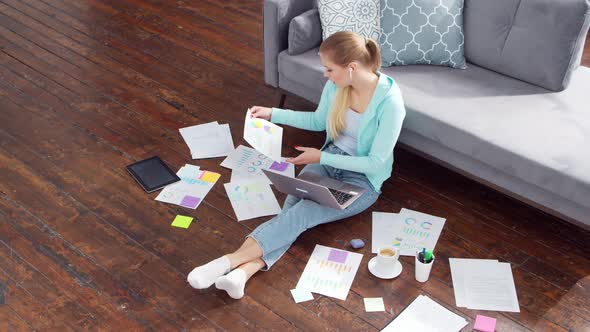 Young woman works with documents using a laptop at home.