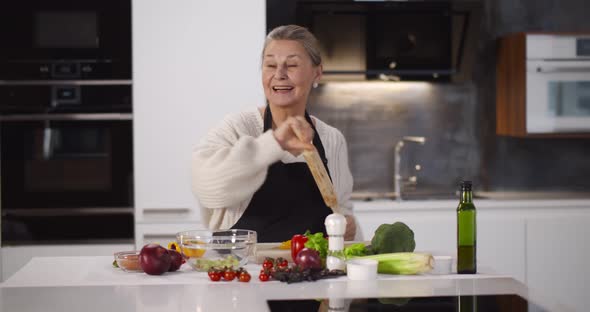 Senior Woman Dancing and Singing While Cooking in Kitchen