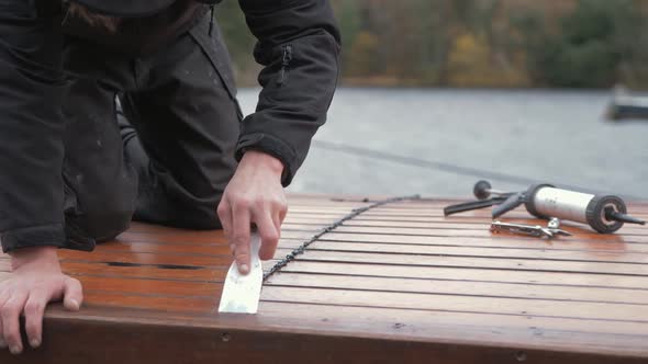 Carpenter repairing cabin roof of boat sealing leaks flattening mastic waterproof sealant.