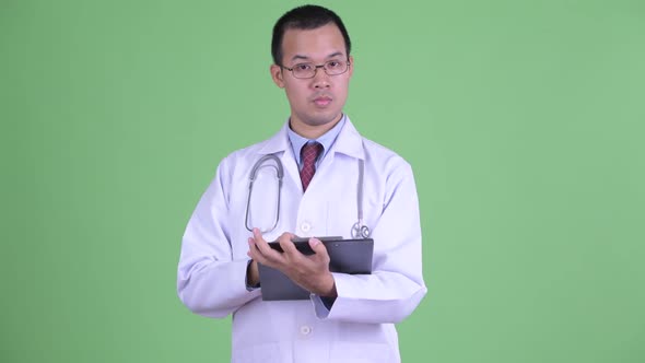 Happy Asian Man Doctor with Eyeglasses Talking While Holding Clipboard