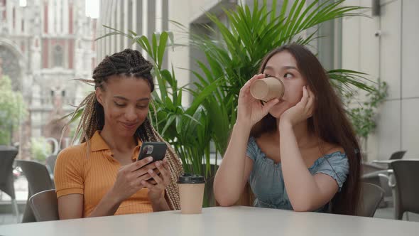 Mixed Race Young Girls Holding Smartphone Use Social Media Asian Woman Drink Coffee in Coffee Shop