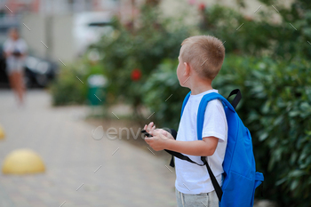 A boy with a briefcase on his back goes to school. Back to school. Safe road to school.