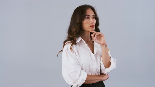 Brunette Model in White Shirt and Black Skirt Has Folded Her Hands and Looking at Something Being