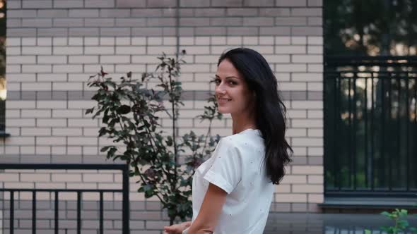 A Cute Young Girl in Jeans and a T-shirt Walks Along a City Street and Looks Straight Inside