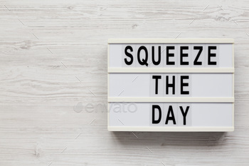 'Squeeze the day' on a lightbox on a white wooden background, overhead view.