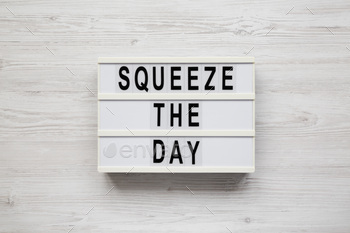 'Squeeze the day' on a lightbox on a white wooden background, overhead view.