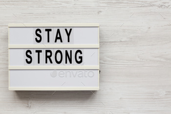 'Stay strong' on a lightbox on a white wooden surface, top view.