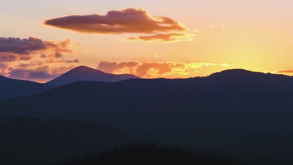 Beautiful Evening Panoramic Landscape with Bright Setting Sun Over Distant Mountain Peaks at Sunset