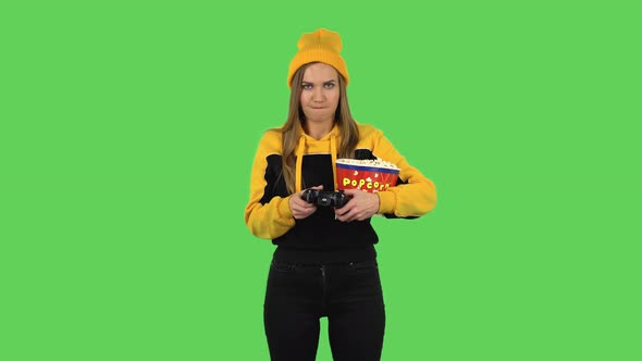 Modern Girl in Yellow Hat with Popcorn Is Playing a Video Game Using a Wireless Controller. Green