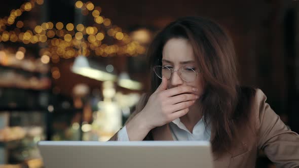 Woman in Jacket Coughing While Sitting at Cafe with Laptop