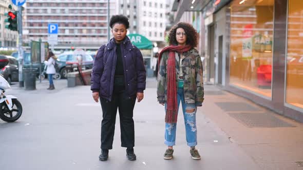 Time-lapse of two multiethnic women outdoor in the city standing looking camera serious