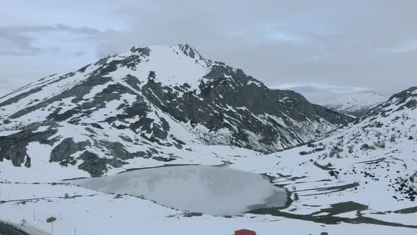 Frozen Lake drone aerial view in the valley of snowy mountains, white cloud sky and enchanted atmosp