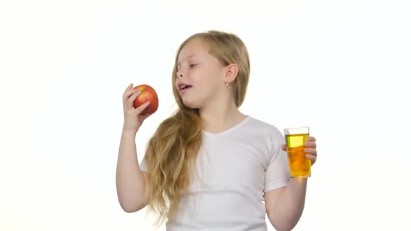 Babies Girl Drinks Juice From a Glass and Holds an Apple. White Background