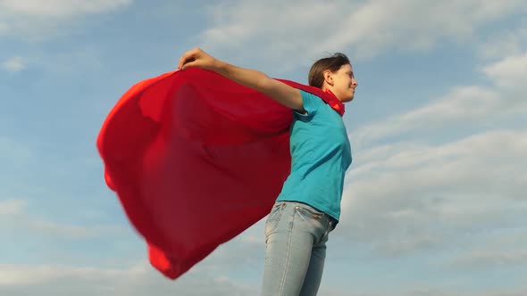 Beautiful Girl Superhero Standing on the Field in a Red Cloak, Cloak Fluttering in the Wind. Slow