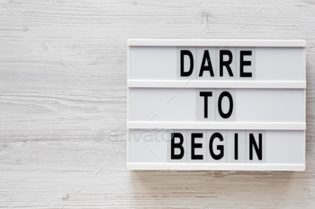'Dare to begin' words on a lightbox on a white wooden background, top view.