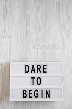 'Dare to begin' words on a lightbox on a white wooden surface, top view.