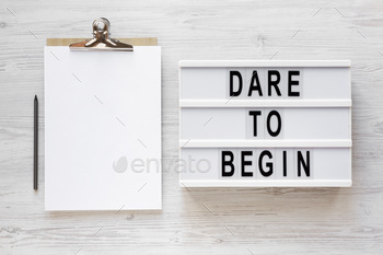 'Dare to begin' words on a lightbox, clipboard with blank sheet of paper.