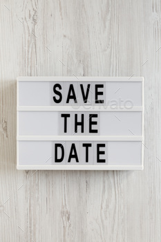 'Save the date' words on a lightbox on a white wooden surface, top view.