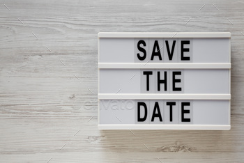 'Save the date' words on a lightbox on a white wooden surface, top view.