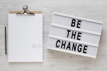 'Be the change' words on a lightbox, clipboard with blank sheet of paper.