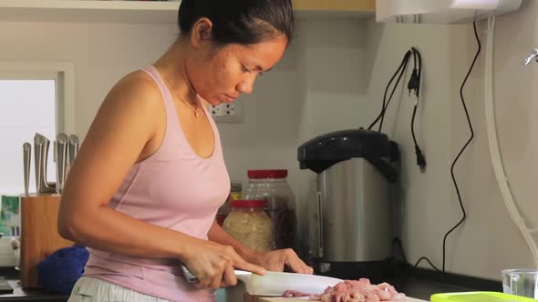 A young woman carefully slicing raw pork meat on a chopping board in the kitchen of her home - Wide