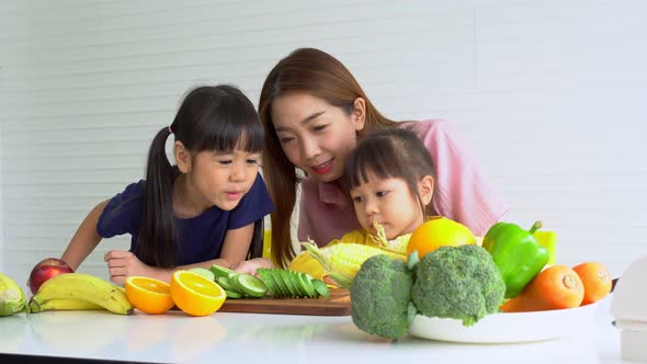Enjoy Asian mom teaching a little daughter holding knife cut fresh vegetables, Happy family mother a