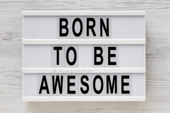 'Born to be awesome' words on a lightbox on a white wooden background, top view.