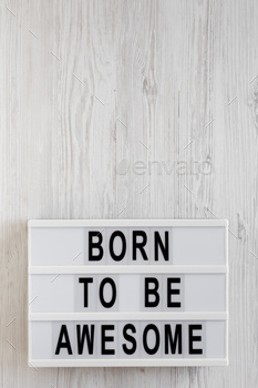 'Born to be awesome' words on a lightbox on a white wooden background, top view.