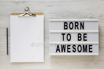 'Born to be awesome' words on a lightbox, clipboard with blank sheet of paper