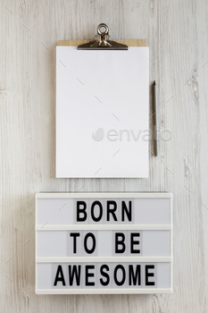 'Born to be awesome' words on a lightbox, clipboard with blank sheet of paper