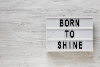 'Born to shine' words on a lightbox on a white wooden background, top view.