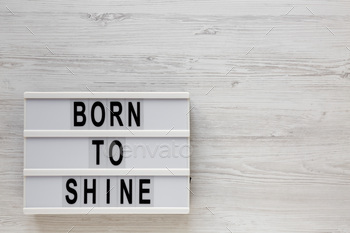 'Born to shine' words on a lightbox on a white wooden surface, top view.