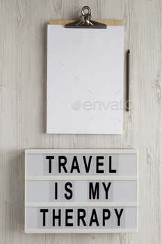 'Travel is my therapy' words on a lightbox, clipboard with blank sheet of paper