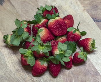a pile of strawberries on top of a wooden cutting board
