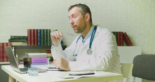 Middleaged Doctor Thinks Through a Research Report While Sitting in a Clinic Office