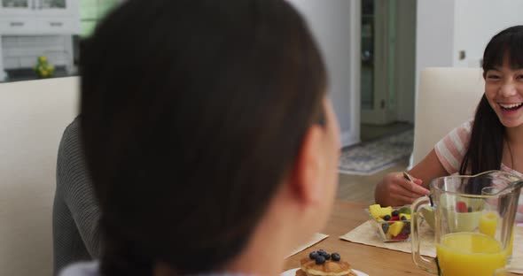 Happy asian parents in kitchen eating breakfast and talking with laughing daughter