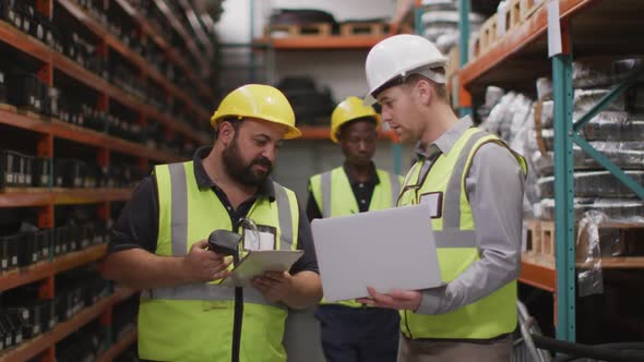 Two Caucasian male factory workers at a factory, wearing vis vests and hard hats, standing