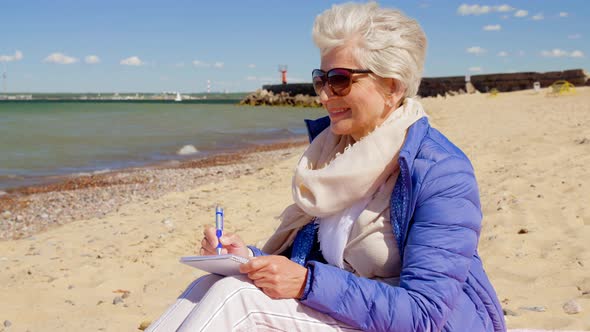 Senior Woman Writing To Notebook on Summer Beach