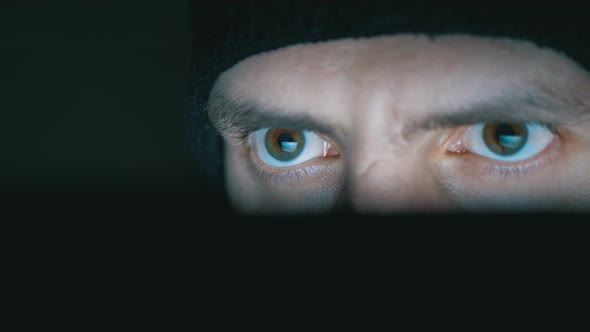 Male in Hat Looks at a Laptop Monitor at Night