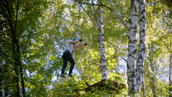 A Man Carefully Walks on the Rope Suspended in the Air Between Trees in the Forest