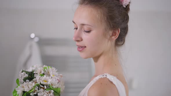 Side View Closeup Portrait of Happy Charming Young Caucasian Bride Admiring White Bridal Bouquet