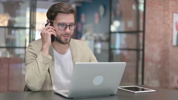 Young Man with Laptop Talking on Smartphone