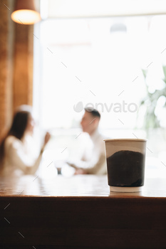 Two People Engage in Conversation Behind Coffee Cup on Wooden Table