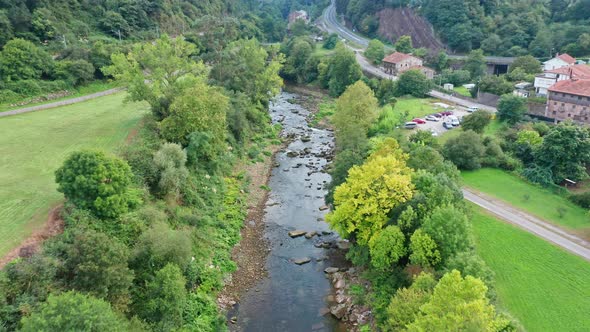 Flying over little river in rural hamlet surrounded by trees in Spain