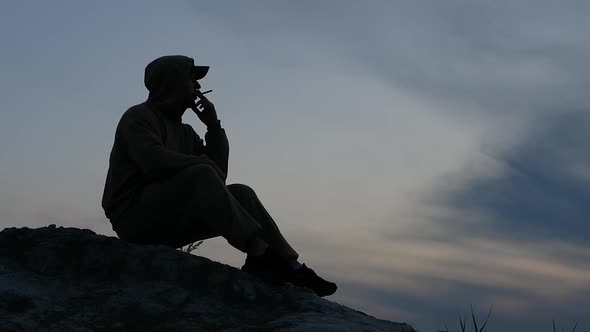 Exhaling Smoke Is Sigratny. Man Smoking A Cigarette On The Top Of A Mountain