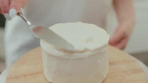 Woman Rotates a Table and Decorates a Birthday Cake with Whipped Cream at Home