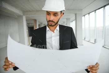 Indian construction site manager standing wearing helmet, thinking at construction site