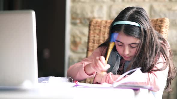 Young Caucasian Girl Doing Homework Using Laptop and Paper