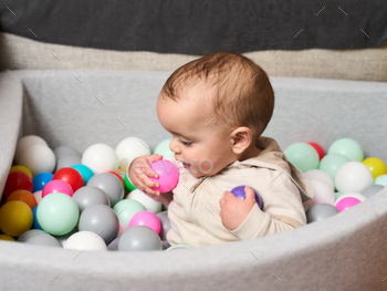 A baby is playing with a ball in a pool of balls