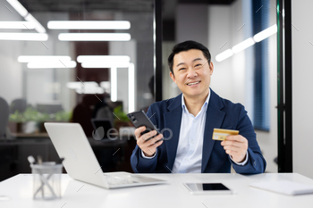 Smiling businessman with credit card and smartphone in office